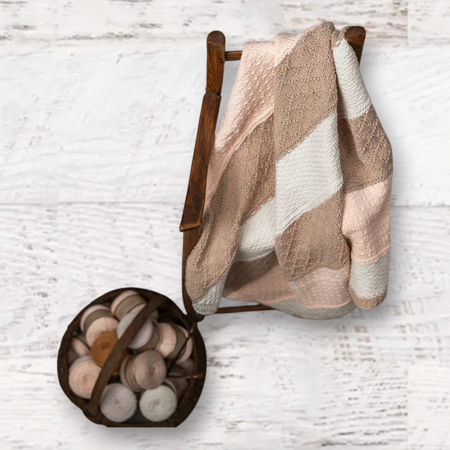 Fuzzy Goat knit baby blanket kit with textured stripes in soft pink, beige, and white draped over a wooden chair.