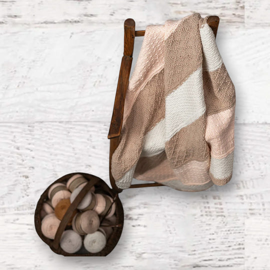 Fuzzy Goat knit baby blanket kit with textured stripes in soft pink, beige, and white draped over a wooden chair.